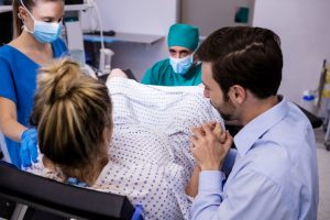 Medical Team Examining Pregnant Woman During Delivery While Man Holding Her Hand