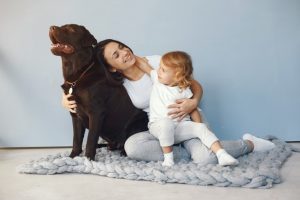 Mother And Little Daughter Playing With Dog At Home